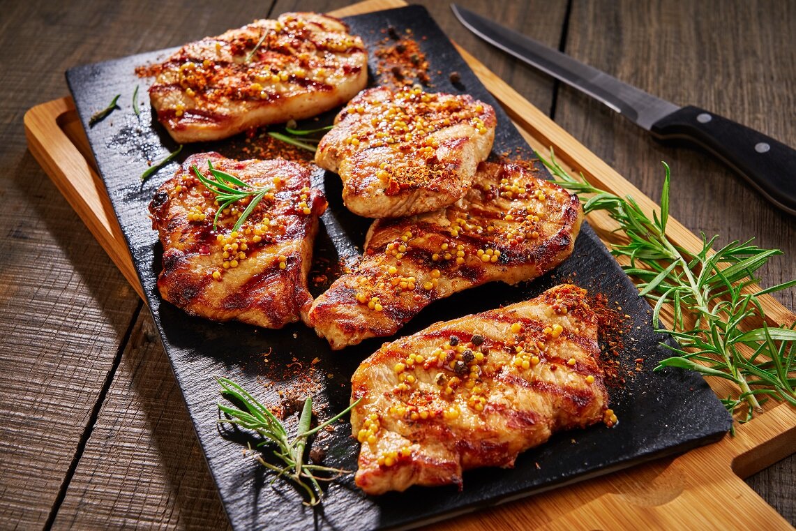 Grilled chicken breasts seasoned with mustard and herbs, served on a black slate platter with fresh rosemary, showcasing a delicious and appetizing meal presentation.
